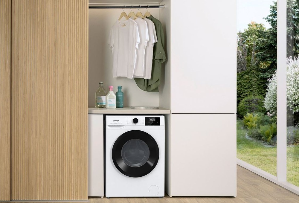 pračka Gorenje W3NGPI74A3S vedle dřevěné skříně. Nad ní visi pradlo na raminku. na boku je videt skleněná stěna na zahradu