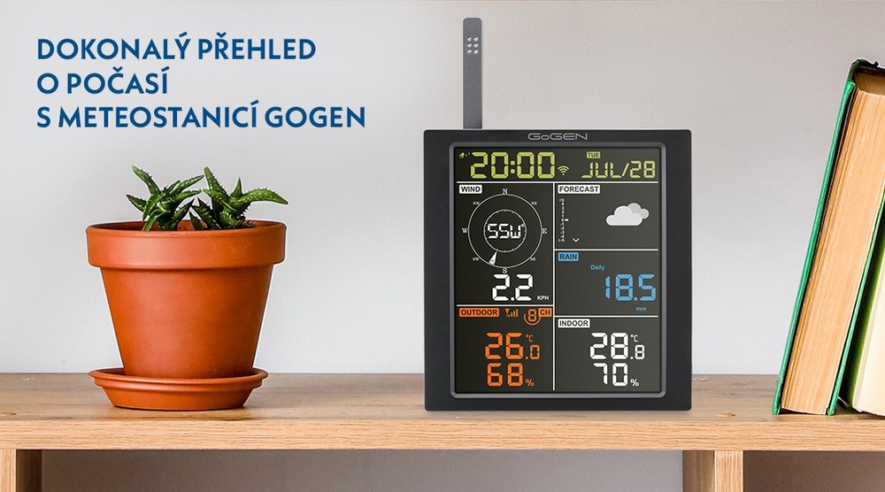 Meteostanice GoGEN ME 3700  s barevným displejem zobrazující detailní informace o počasí, včetně času, vnitřní a venkovní teploty, vlhkosti, rychlosti větru a srážek umístěná na dřevěné polici s knihami a pokojovou květinou