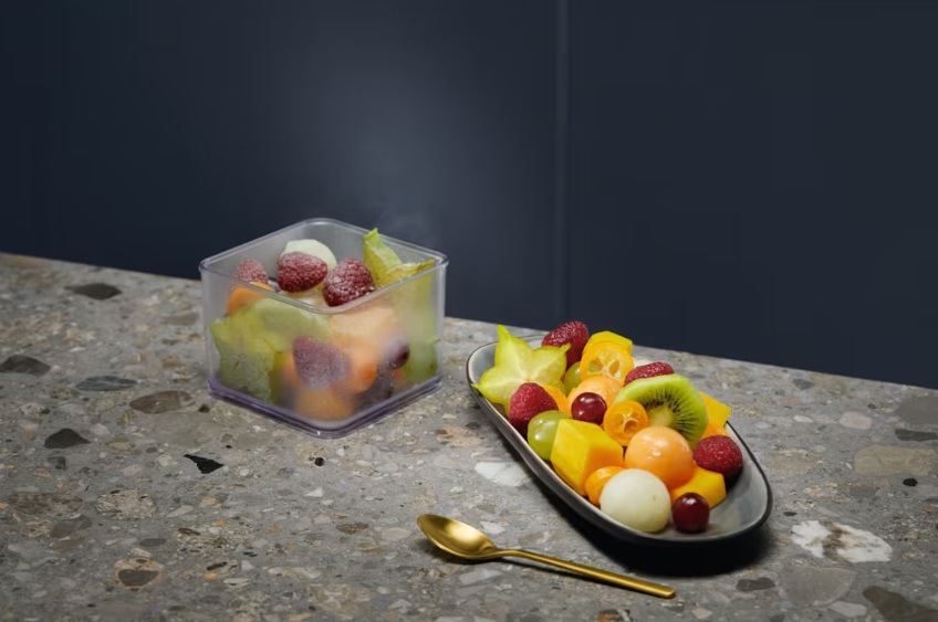 Zmrzlé ovoce v plastové nádobě. Rozmrzlé ovoce na talíři, vedle něj je lžička.