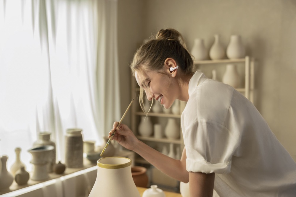 Sluchátka Shokz OpenDots 2, Bluetooth bílá Žena s otevřenými sluchátky malující keramickou vázu