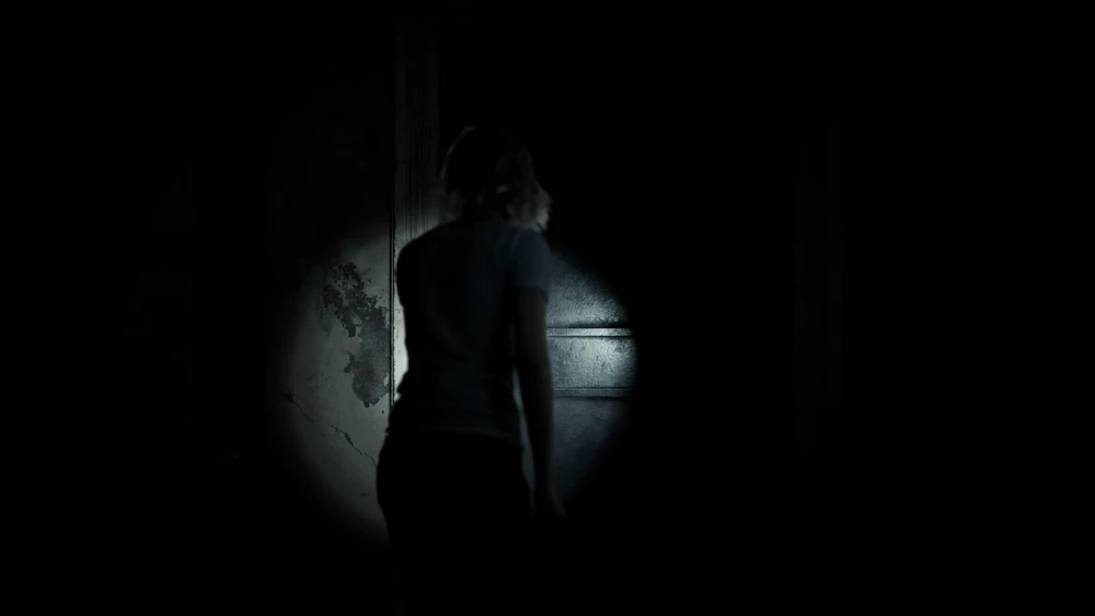Temná atmosférická scéna ze hry Resident Evil Requiem. Na obrázku je hlavní hrdinka obklopená temnotou, kterou prosvětluje pouze kužel baterky, jež drží v ruce.