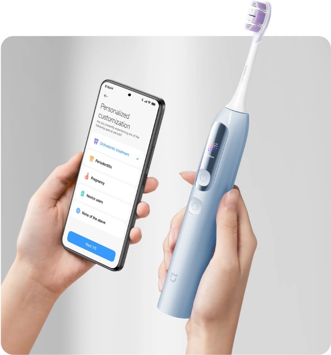 Ruce drží modrý elektrický zubní kartáček Xiaomi MES613 a chytrý telefon s otevřenou obrazovkou pro přizpůsobení nastavení čištění