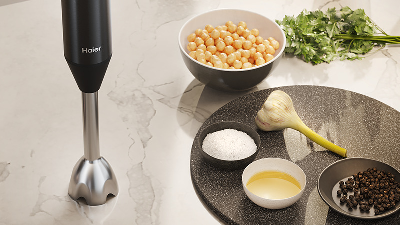 Ponorný mixér Haier HHB5B2/1 011 stojí na stole vedle misek s ingrediencemi