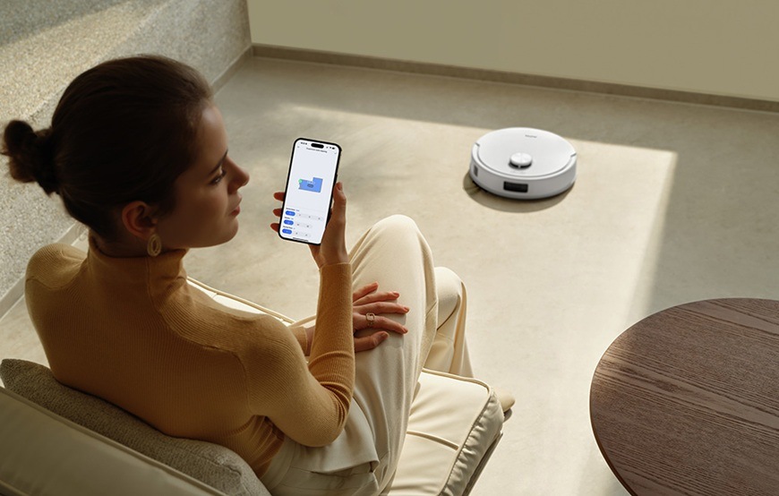 Detail obrázku muže ovládající robotický vysavač pomocí mobilní aplikace.