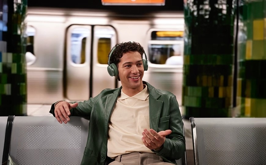 Muž sedící na lavičce v metru telefonuje se sluchátky JBL Live 680NC vybavenými potlačením šumu