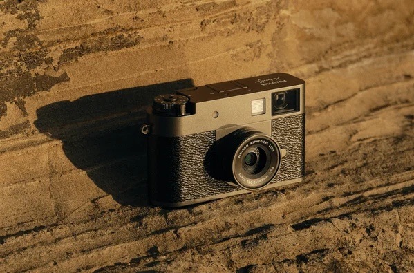 Digitální fotoaparát Fujifilm X half stříbrný Kompaktní fotoaparát Fujifilm X half opřený o kamennou zeď, zvýrazňující retro vzhled a pevnou konstrukci
