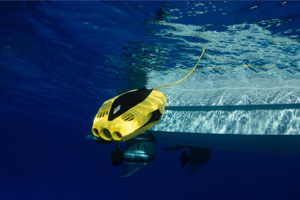 Žlutý podvodní dron Chasing Dory pluje pod hladinou u lodního šroubu a je propojený žlutým signálním kabelem.