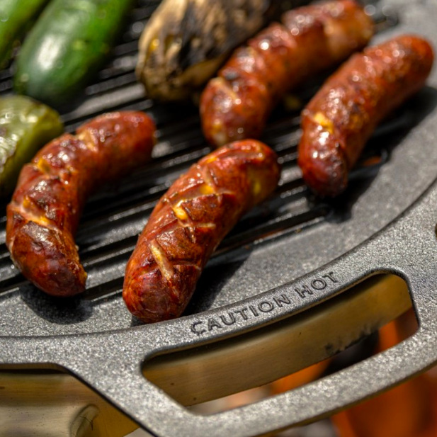 Detail litinového roštu Solo Stove Yukon 27 s klobásami a označením Caution Hot na madle