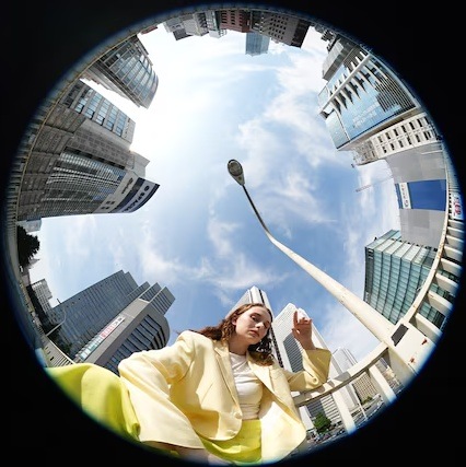 Objektiv Sony FE 8-14mm f/3.5 Fisheye G černý Pohled vzhůru na ženu mezi mrakodrapy s výrazným kruhovým zkreslením objektivu