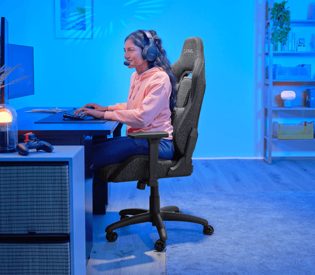 Žena se sluchátky sedící u herního stolu na židli Trust GXT 723 RUYA Fabric