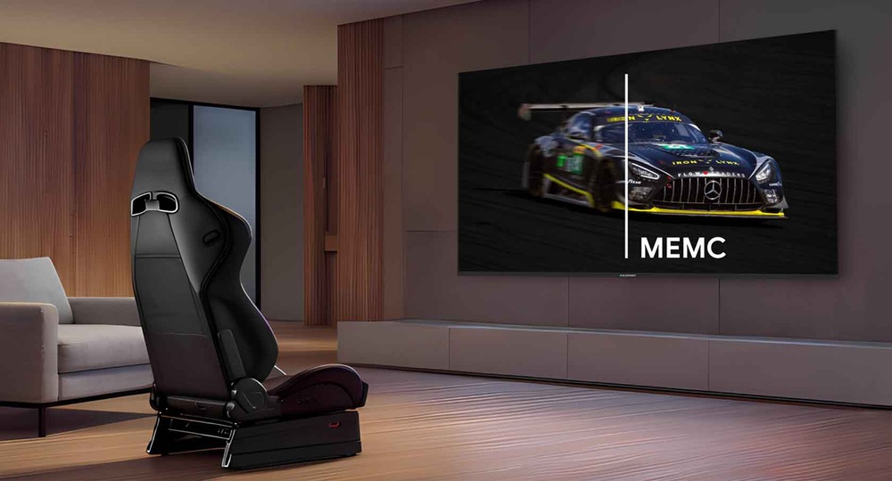 Elegantní, moderní místnost s křeslem v závodním stylu s velkou plochou obrazovkou zobrazující závodní auto. Obrazovka ukazuje technologii „MEMC“ v akci.