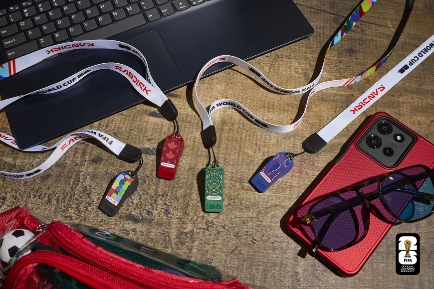 USB Flash SANDISK USB-C Flash Drive FIFA World Cup 2026 64GB černý Kolekce USB flashdisků SanDisk FIFA World Cup 2026 položená vedle notebooku a telefonu