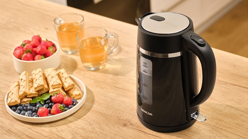 Rychlovarná konvice Sencor SWK 2710BK, 1,7 l černá Rychlovarná konvice Sencor SWK 2710BK je položená na kuchňské lince a vedle ní je talíř s pochutinami.