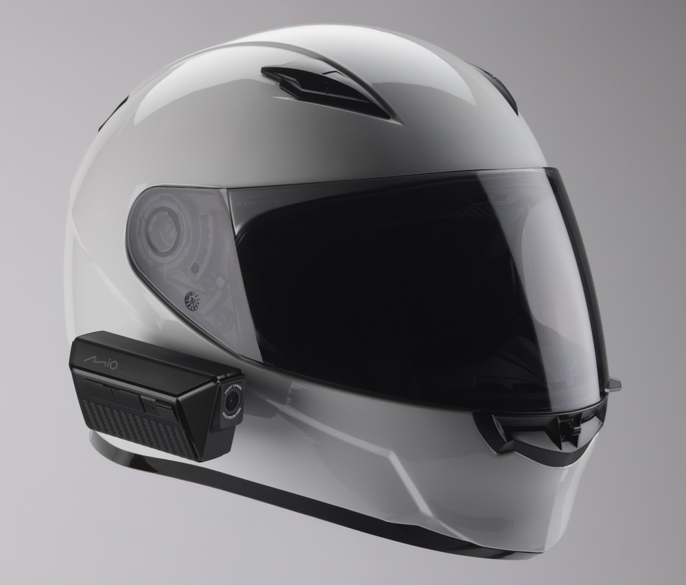 Motokamera Mio MiVue MP20 černá Černá motokamera Mio MiVue MP20 upevněná na levém boku bílé integrální přilby. Přední objektiv směřuje ve směru jízdy, zatímco podlouhlé tělo kamery kopíruje spodní hranu přilby. Obrázek znázorňuje způsob umístění zařízení při používání.