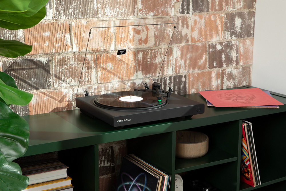 Gramofon Victrola VPT-1520 Wave umístěný v moderním interiéru na skříňce, přehrává vinylovou desku v obývacím pokoji