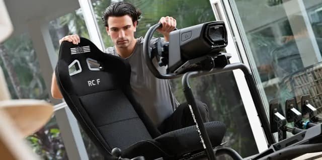 Závodní kokpit Next Level Racing RC FOLDABLE Simulator Cockpit černý V prosvětlené místnosti si soustředěný muž nastavuje běžecký pás; drží se jeho ovládacího panelu a bočního krytu, zatímco sluneční světlo proniká dovnitř velkými okny.