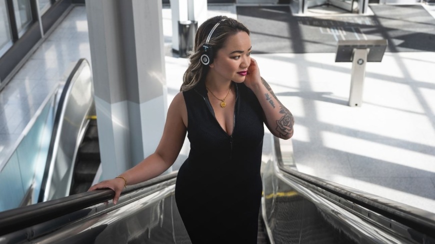 Žena jedoucí po eskalátoru poslouchá hudbu ze sluchátek Koss Porta Pro Wireless 2.0