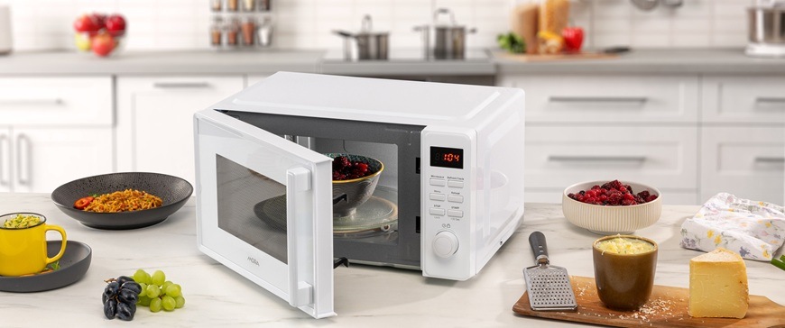 Na obrázku je pootevřená mikrovlnná trouba Mora MT323W v bílé barvě a kolem ní je položené jídlo