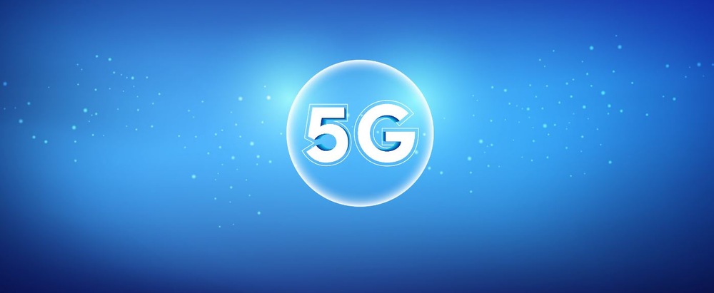 Modré pozadí s textem „5G“ tučným bílým písmem uvnitř zářící, průsvitné koule. Kouli obklopují malé světelné částice, které navozují futuristický a digitální dojem.