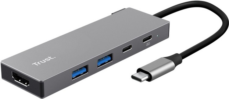 USB Hub Trust DALYX 5v1 stříbrný Na obrázku je stříbrný USB-C hub Trust DALYX 5v1 zachycený šikmo zepředu. Má úzké kovové tělo s čistým hranatým designem a z jednoho konce z něj vede krátký černý kabel zakončený USB-C konektorem. Na levém čele je HDMI konektor, na boku dva modře značené USB porty a dva menší USB-C porty, vedle nichž je malá kontrolka.