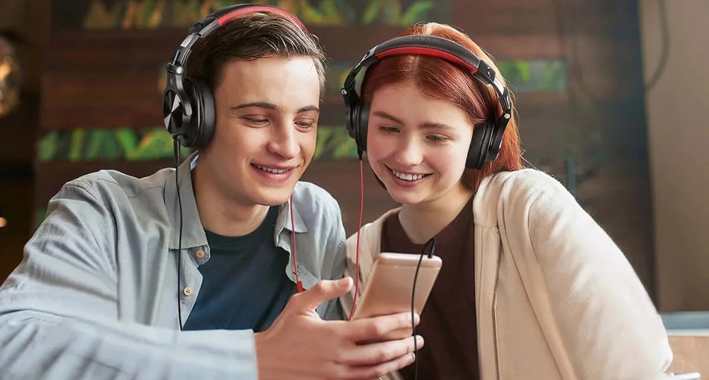 Sluchátka OneOdio Fusion A71M DJ náhlavní s odpojitelným Boom mikrofonem černá Muž a žena společně sledují obsah na telefonu díky sluchátkům OneOdio Fusion A71M se sdílením zvuku