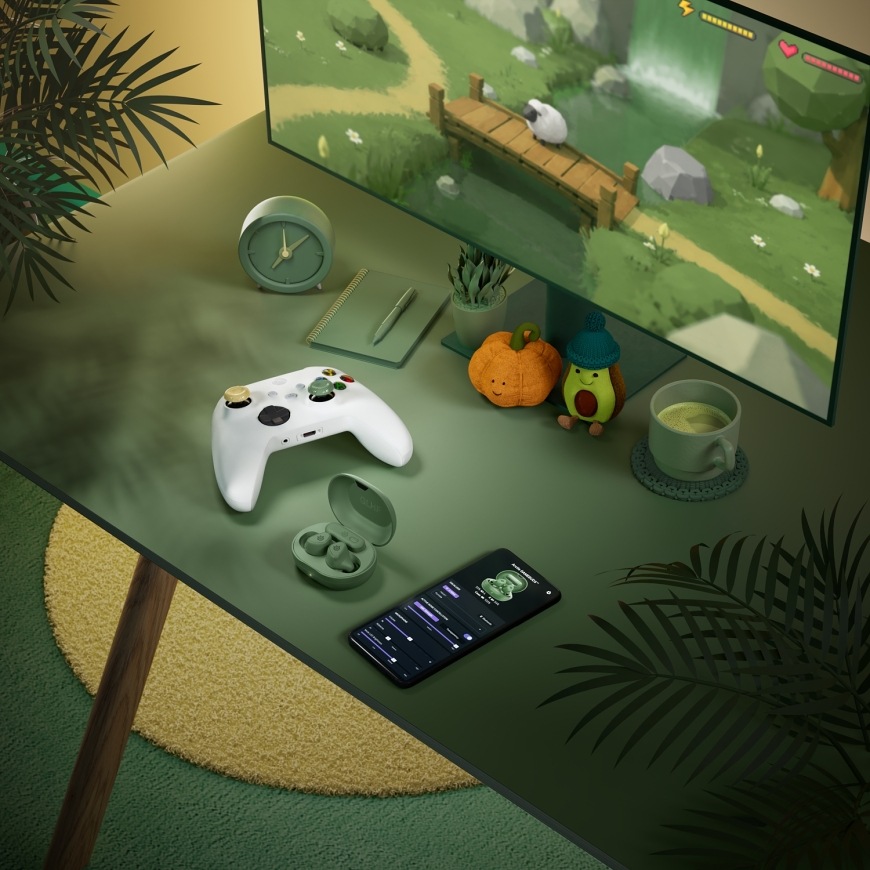 GameBuds Matcha na herním stole s ovladačem Xbox a mobilní aplikací na telefonu