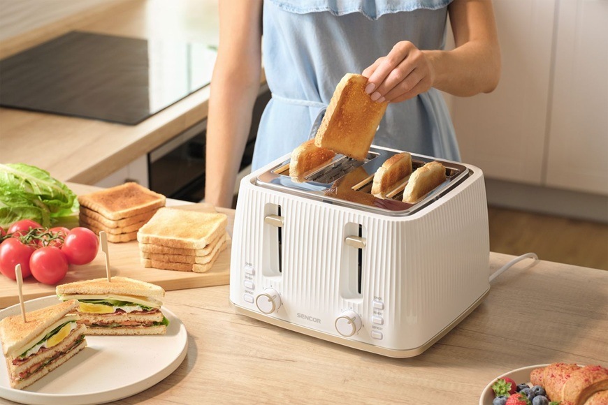 Topinkovač Sencor STS 7540WH bílý Žena připravuje snídani a vytahuje toast z topinkovače Sencor STS 7540WH v moderní světlé kuchyni.