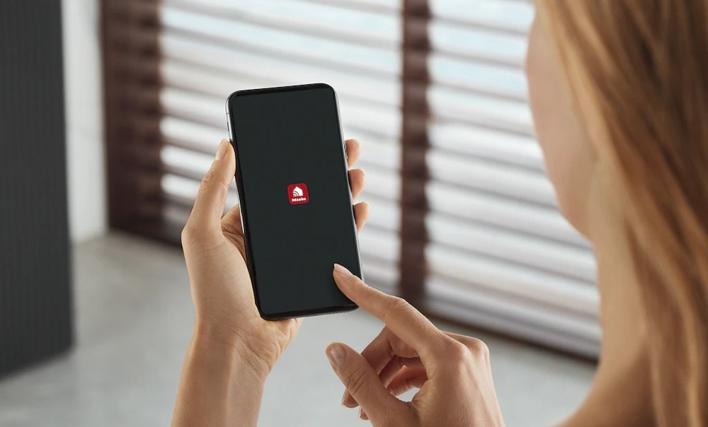 Vinotéka Miele KWTS 4785 F černá Ruce drží mobilní telefon, na jehož displeji je aplikace Miele