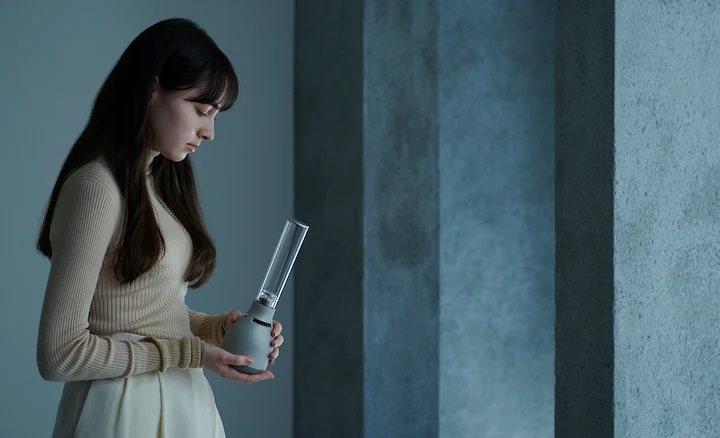 Přenosný reproduktor Sony LSPX-S3 stříbrný/šedý Mladá žena drží skleněný reproduktor Sony LSPX-S3 a demonstruje jeho kompaktní rozměry.