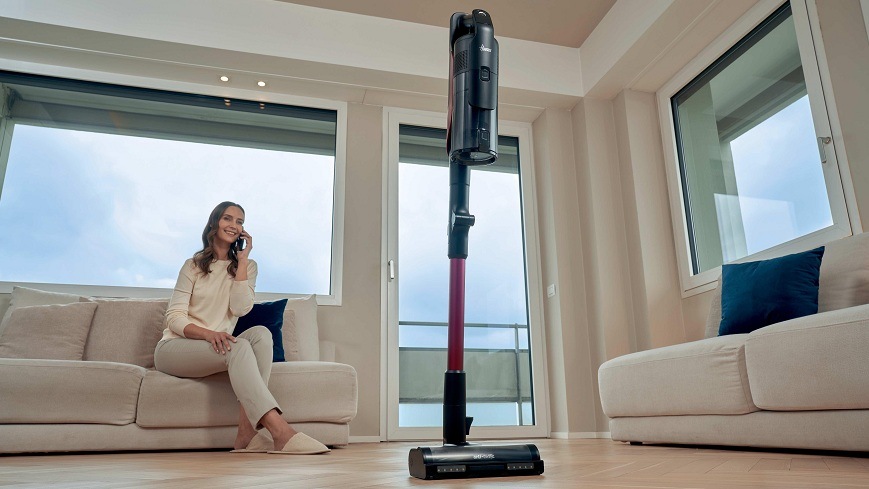 Tyčový vysavač Hoover HF610HX 011 černý Tyčový vysavač Hoover HF610HX 011 stojí uprostřed místnosti, zatímco žena na gauči telefonuje