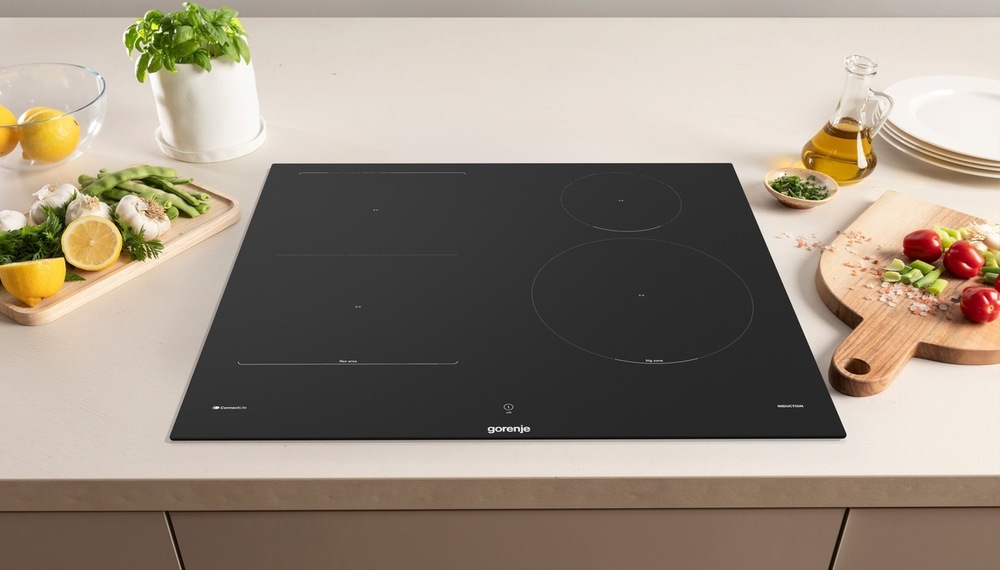varná deska Gorenje GI6433SRWF na světle kuchynské desce. Vedle ní je ovoce a zelenina na dřevených prkýnkách