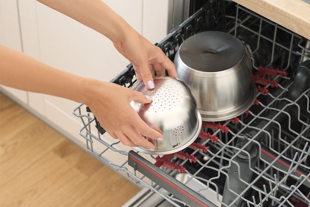 Rýžovar Sencor SRM 2000WH Low Carb Žena dává nerezový košík z rýžovaru do myčky nádobí