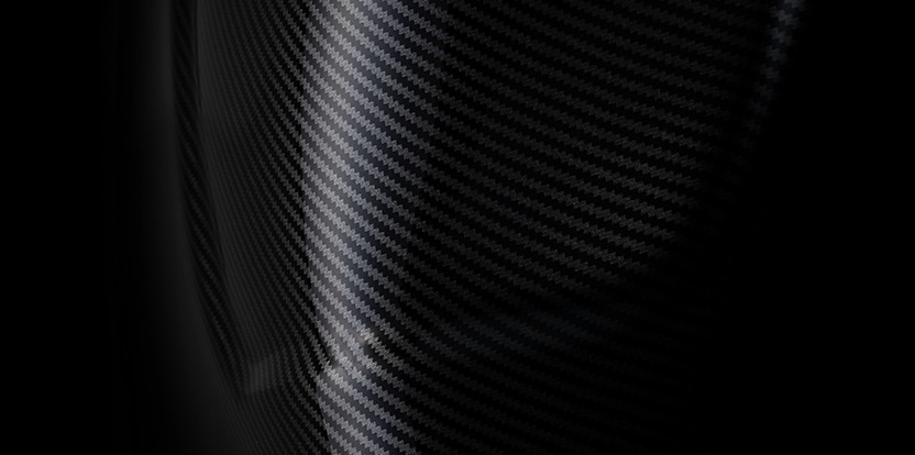 Detail zakřiveného, lesklého povrchu z uhlíkových vláken, na kterém jsou vidět diagonální vzory a jemné odrazy světla. Obrázek vyzařuje elegantní, moderní dojem.