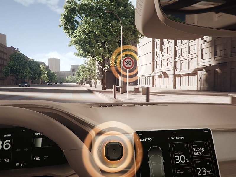 Pohled z automobilu na městskou ulici s rychlostním omezením 30 km/h. Cestovní asistent TomTom Tom na palubní desce svítí oranžovým LED kroužkem a upozorňuje řidiče na překročení povolené rychlosti.