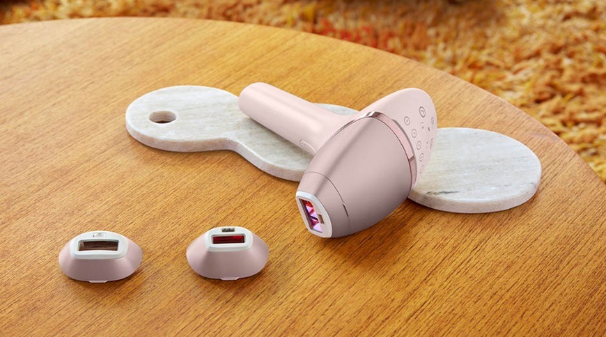 Epilátor Philips BRI953/02 Lumea IPL 9900 SkinAI je položen i s nástavci na konferenčním stolu.