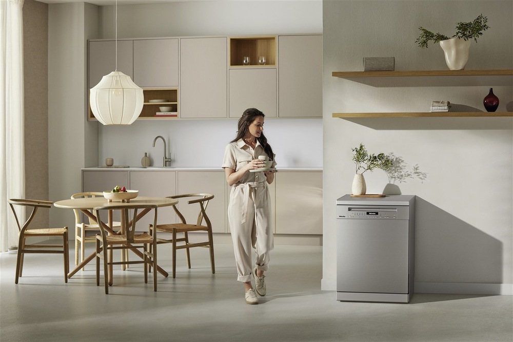 Myčka nádobí Miele G 7040 SC AutoDos nerez Žena stojí v kuchyni, drží v rukou šálek a dívá se na myčku nádobí Miele G 7040 SC AutoDos