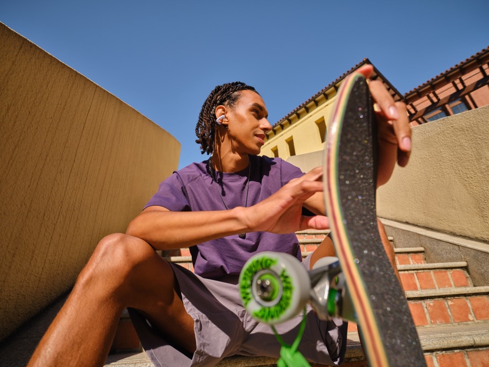 Sluchátka Shokz OpenDots Air, Bluetooth fialová Muž sedící se skateboardem a sluchátky Shokz OpenDots Air v uších