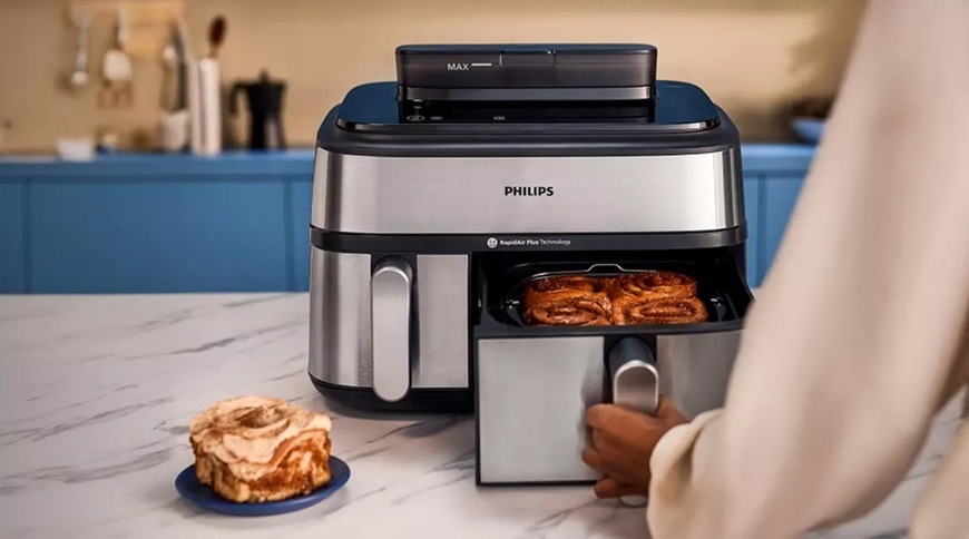Fritéza horkovzdušná Philips Airfryer Dual Basket 5000 series 9 l, NA555/00 stříbrná Žena drží madlo u většího koše a povysouvá ho směrem k sobě. V pozadí je vidět zbytek kuchyňské linky.