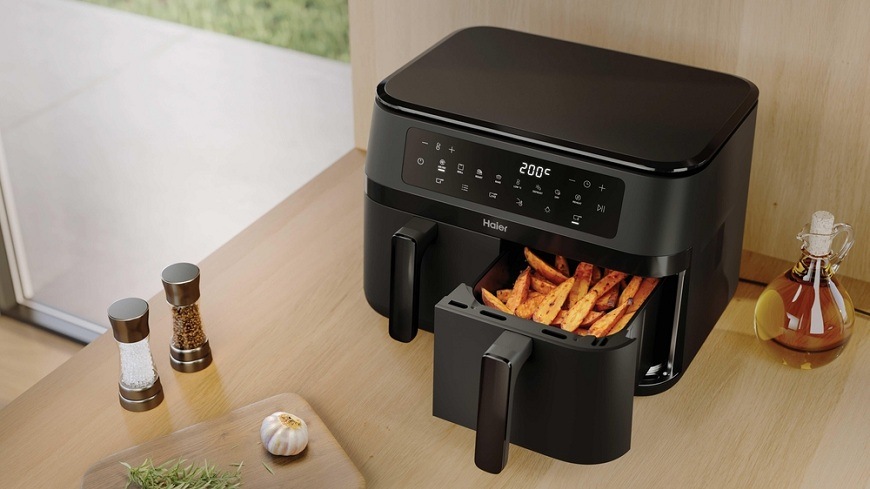 Horkovzdušná fritéza Haier HAF3AD 011 na kuchyňské lince, vedle ní se nachází ingredience, jeden koš je otevřený a jsou v něm hranolky