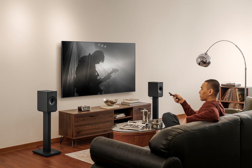 Reproduktory KEF Coda W (2 ks) černé Muž sleduje koncert na televizi doplněné po stranách o reproduktory