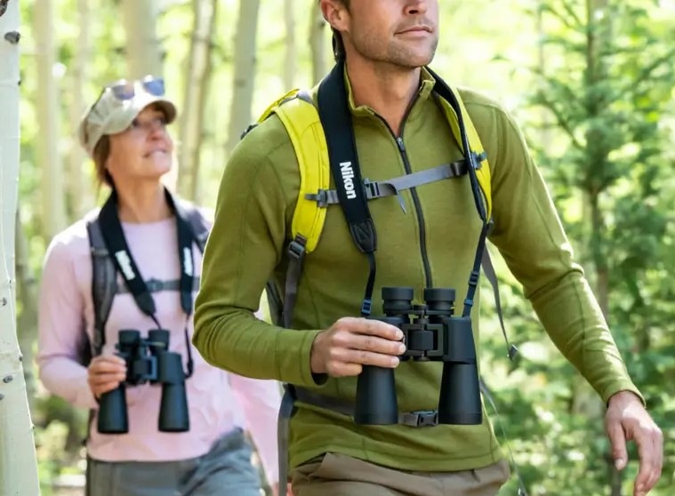 Dalekohled Nikon Action 10×50 černý Muž se ženou jdou lesem, každý má na krku dalekohled Nikon Action 10×50, který zároveň drží jednou rukou.