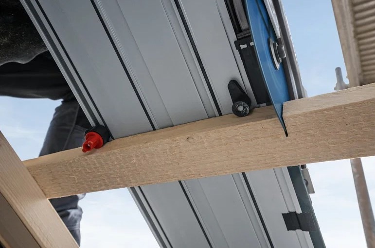 Detailní pohled zespodu na okružní pilu Bosch Professional GKS 18V-57-2 GX s vodicí lištou při řezu.
