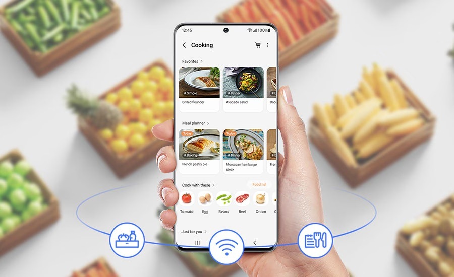 Americká lednice Samsung RF24BB620EB1EO černá Ruka drží mobilní telefon s aplikací SmartThings Food, na pozadí jsou krabice s potravinami