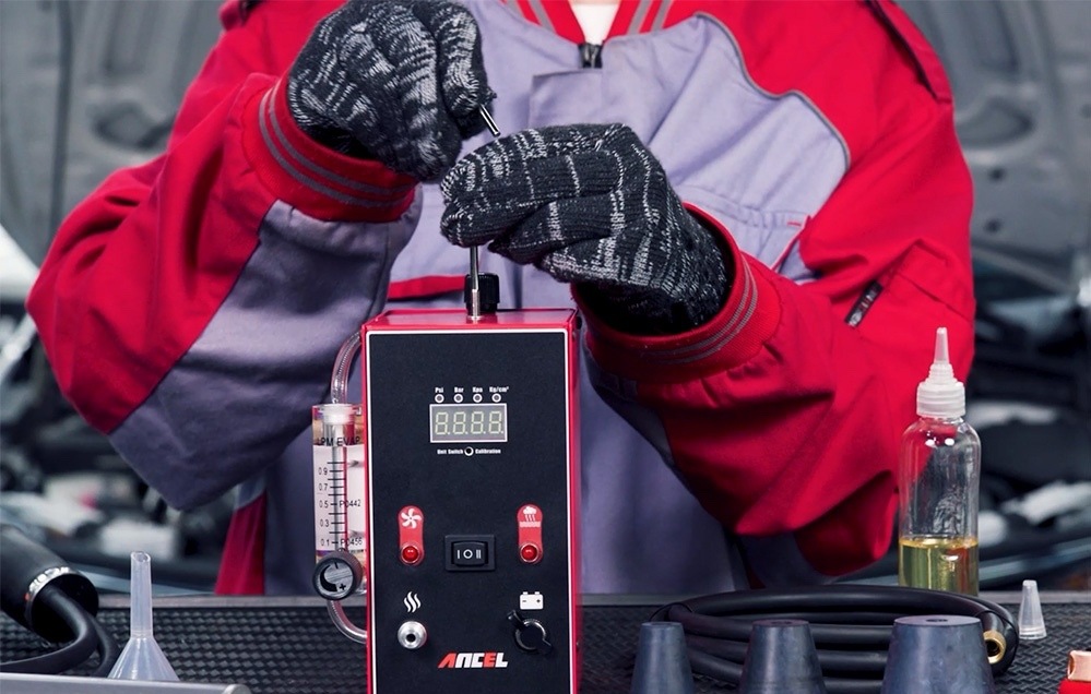Diagnostika vozu Ancel L300 černá Technik při plnění diagnostiky úniků Ancel L300 testovacím olejem, vedle přístroje jsou hadice a kuželové adaptéry.