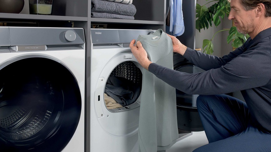 Sušička prádla Haier HD90-AQ387U1-S bílá muž vyndavá ze sušičky Haier HD90-AQ387U1-S suché oblečení a prohlíží si šedý svetr