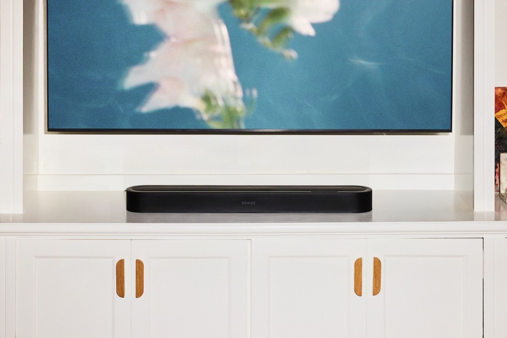 Černý soundbar Sonos Beam Ultra umístěný na bílé TV skříňce pod televizí v obývacím pokoji.