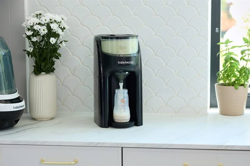 Baby Brezza Formula Pro Advanced Black s kojeneckou lahvičkou stojí na čisté pracovní desce v kuchyni.