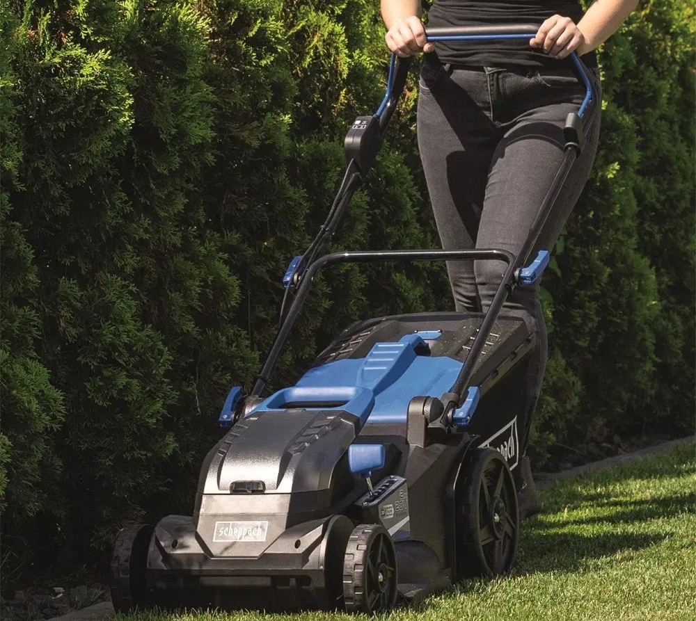 Pohled na akumulátorovou sekačku Scheppach BC-MP430-X-SET XL2 při sečení trávníků podél stromů.