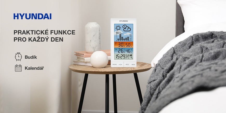 Meteorologická stanice Hyundai WS 2050 bílá Bílá meteorologická stanice Hyundai s funkcí budíku a kalendáře na dřevěném nočním stolku vedle postele ukazující naměřené hodnoty