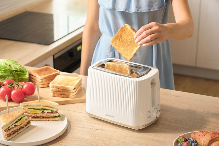 Topinkovač Sencor STS 7510WH bílý Žena dává toast do topinkovače Sencor STS 7510WH. Na lince jsou topinky, toasty, rajčata a salát.